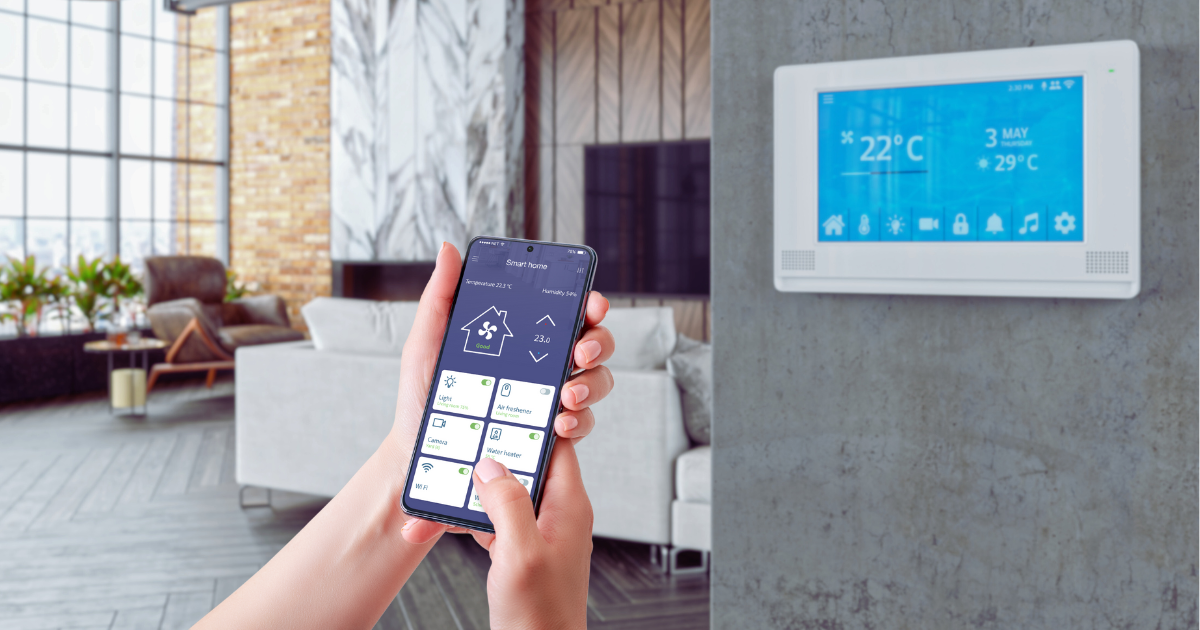 A person holding a smartphone displaying their IAQ monitoring system, connected to a smart thermostat for real-time indoor air quality control.